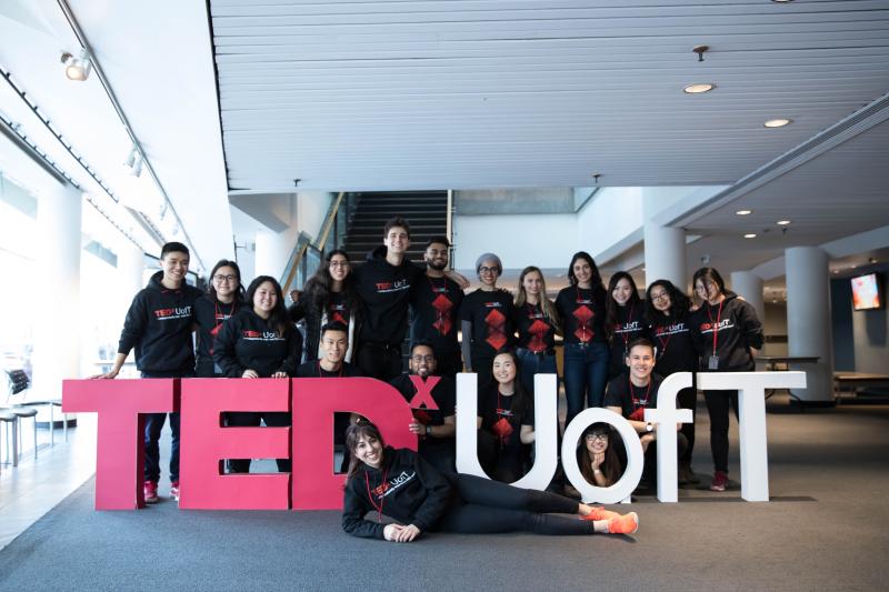 A large group of happy students in matching t-shirts pose with a big sign: TEDx U of T.