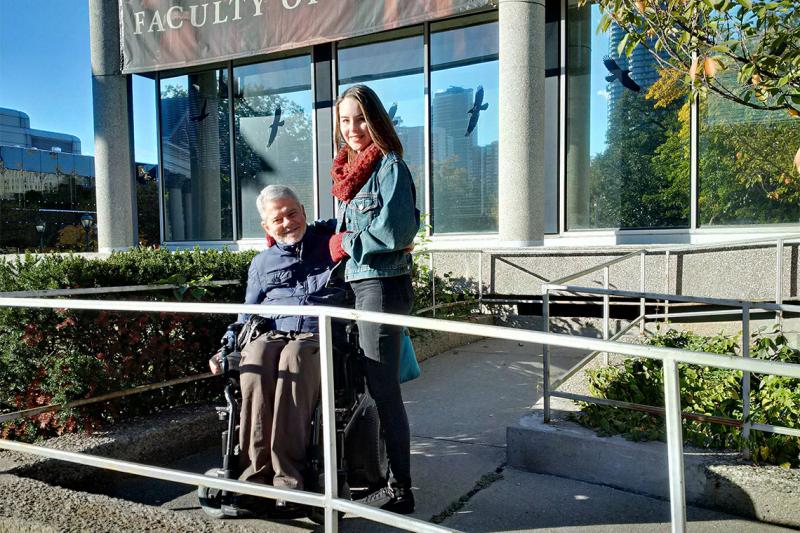 Ian Parker smiles as he poses in his wheelchair on a ramp, with his arm around his daughter Emily Parker (who is standing).