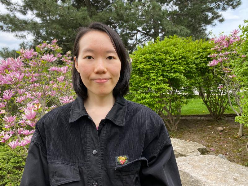 Irene Fang stands outside with trees and flowers around her