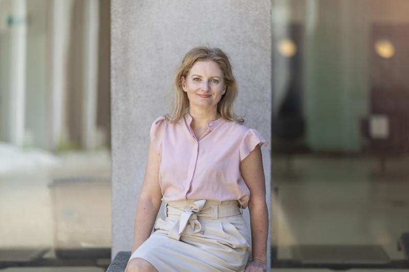 Jennifer Gommerman smiles, sitting in front of a concrete pillar outdoors.