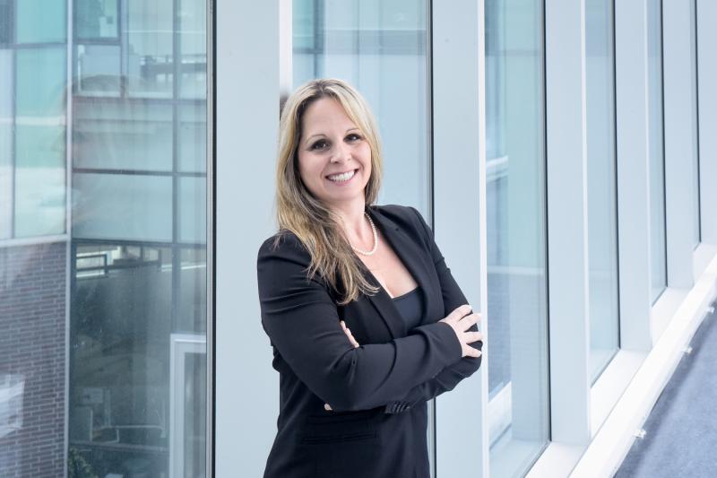 Julie McCarthy smiles, standing in a glass-walled walkway.