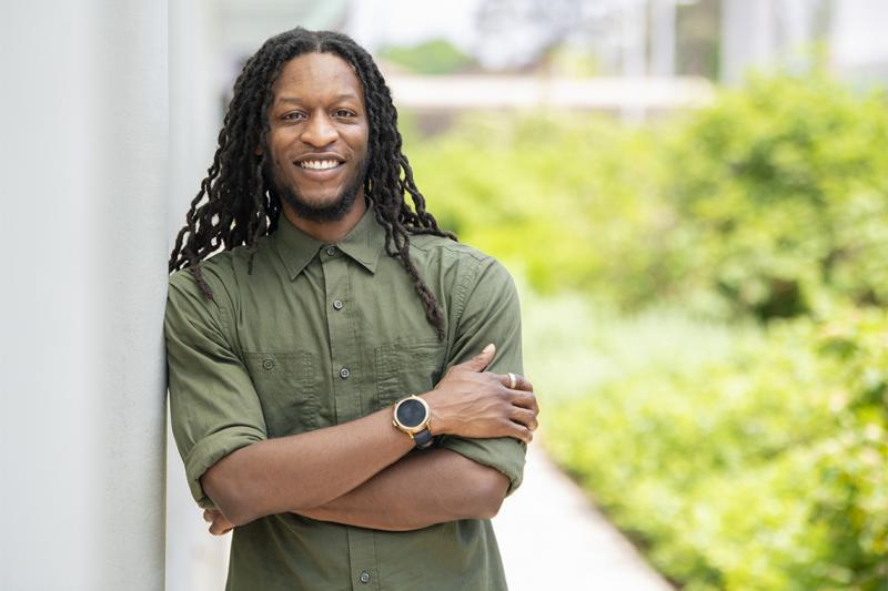 Kadeem Daley-Lewis smiles as he leans on a wall next to a garden.