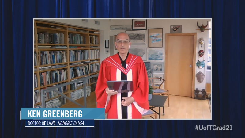 Ken Greenberg, wearing academic robes, speaks in a room decorated with bookshelves, paintings, and carved masks.