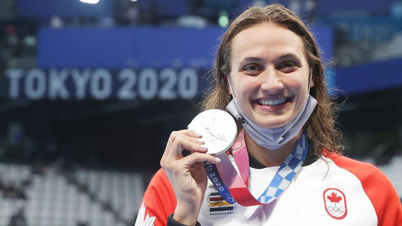 Kylie Masse smiles as she holds up her Olympic silver medal. A banner behind her reads: Tokyo 2020.