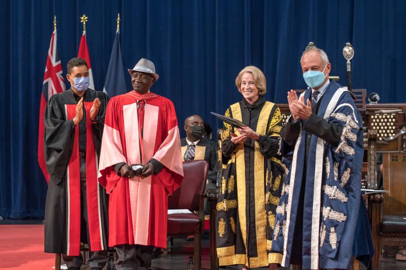 Meric Gertler and Rose Patten applaud Winston LaRose on stage in Convocation Hall. All three wear academic robes.