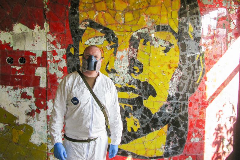 Major Gary Johnston wears a gas mask and environmental boiler suit as he stands by a mural in an abandoned building.