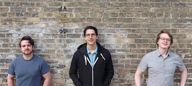 Chris Leichthammer, Aidan Tinafar and Alex Klenov smile as they pose in front of a brick wall.