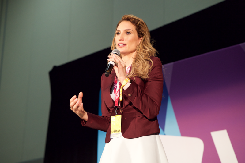 Lorraine D'Alessio stands on a stage, giving a presentation.