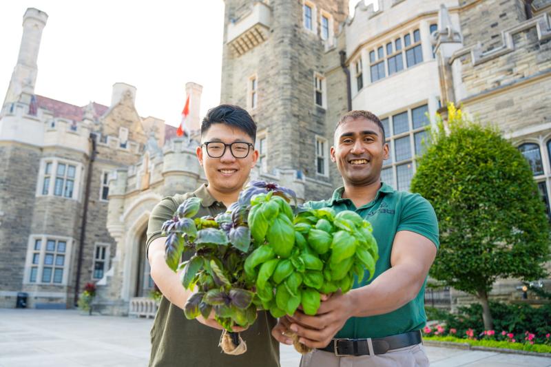 Leo and Adnan holding basil plants in front of the Casa Loma building