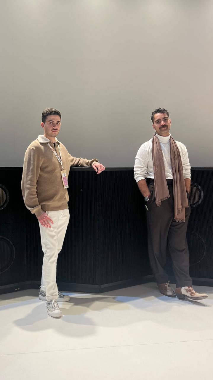 A portrait of two people standing next to waist-high black speakers