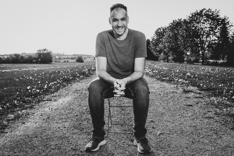 Mark Crawford sitting on a stool in the middle of a field, laughing.