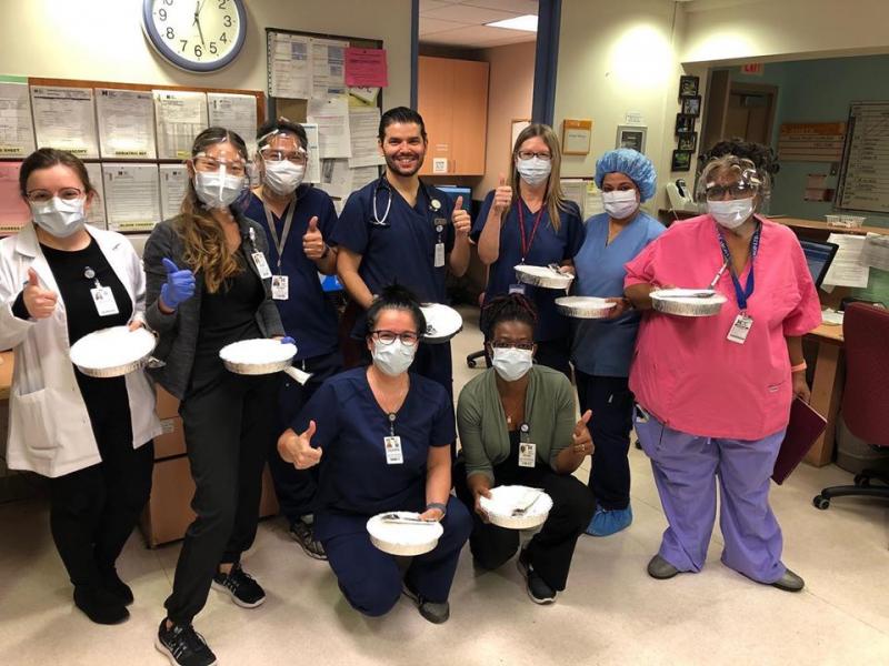 A group of hospital workers in masks, gloves and scrubs hold out trays of delivered meals.