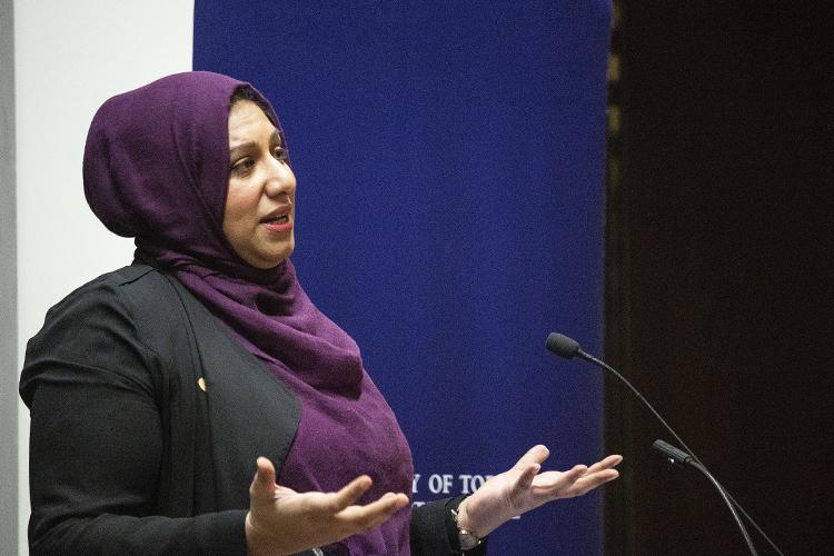 Ausma Malik holds both hands palms up as she gestures while speaking at a podium.