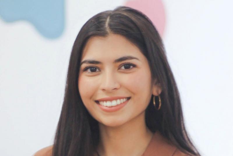Nuha Siddiqui smiles as she stands in front of a display of colourful abstract shapes.