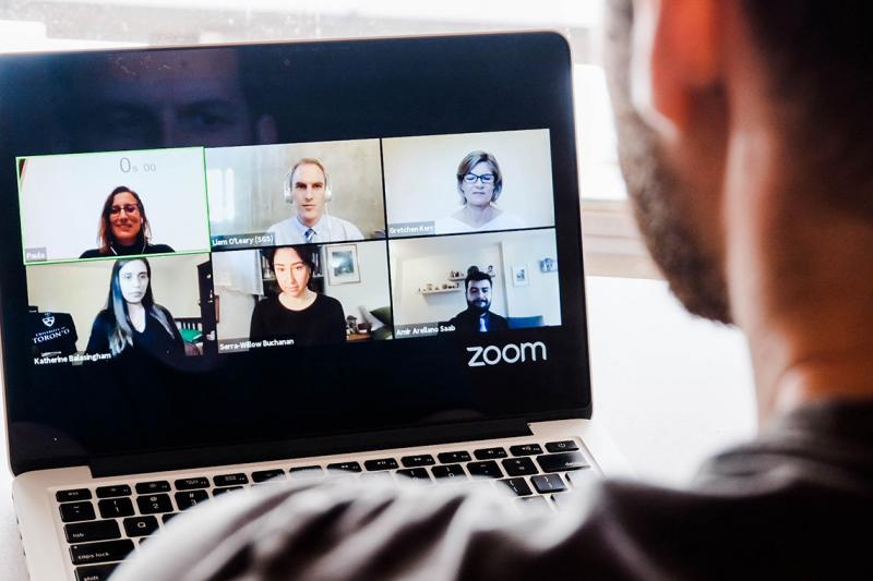 A man looks at a laptop which is running a video chat application with six other users.