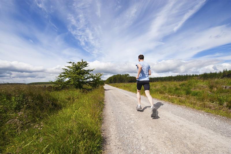 A man jogs along an empty country road under a wide sunny sky.