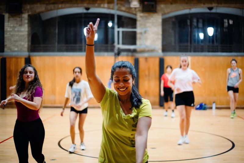 Sandani Hapuhennedige smiling in a gymnasium as she teaches a fitness class to others.