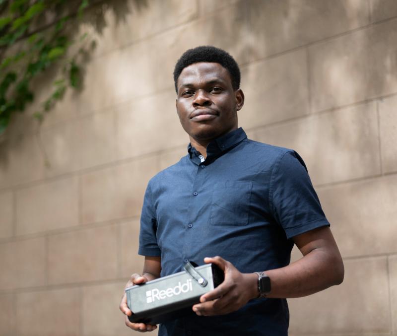 Olugbenga Olubanjo smiles as he holds a loaf-sized black box with the word Reeddi on the side.