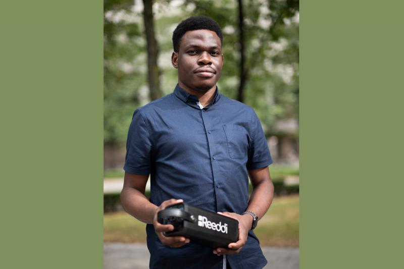 Olugbenga Olubanjo stands outside by trees, holding a loaf-sized, rectangular box with the word Reeddi on the side.