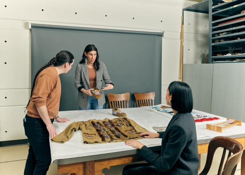 Three people at a large table with traditional Indigenous garments on it