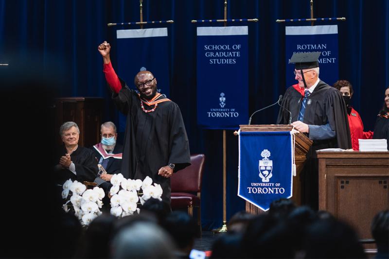 A smiling graduate pumps his fist on the stage at Rotman, while other officials look on