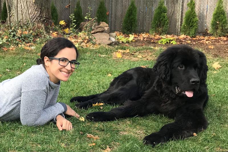 Sofia Bonilla smiles happily as she lies on a grass lawn with her very large Newfoundland dog, Snuffie.