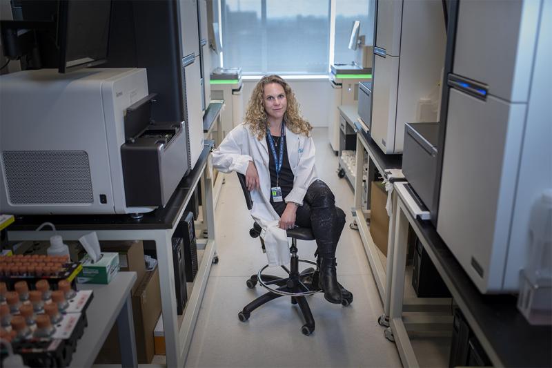 Lisa Strug sits on a chair between fridges and other lab equipment.