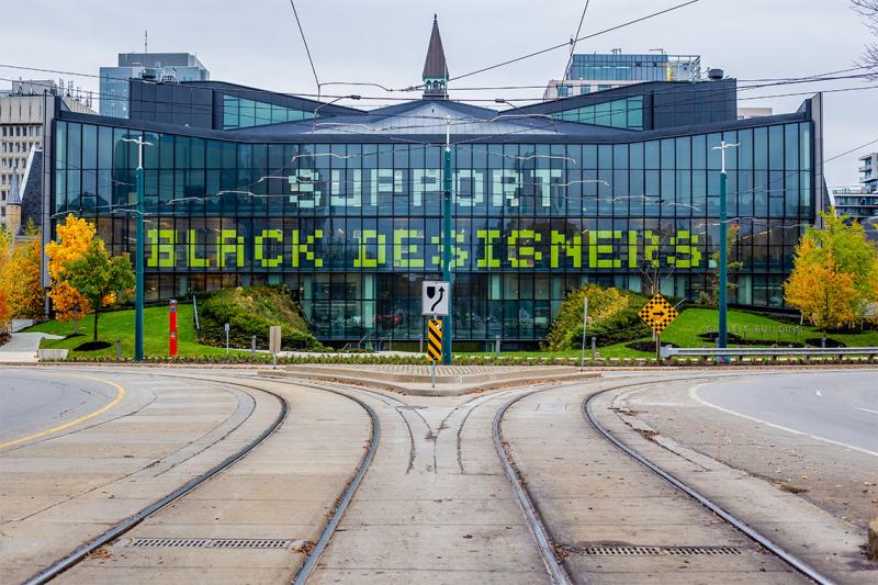 The words Support Black Designers are spelled out across the glass windows of the modern half of One Spadina.