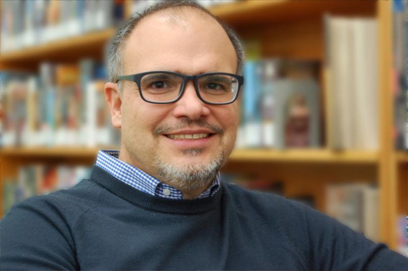 A portrait of Teo Salgado smiling in front of a bookshelf.