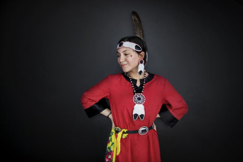 Dancer Miyopin Cheechoo wears traditional clothing, including a large feather.