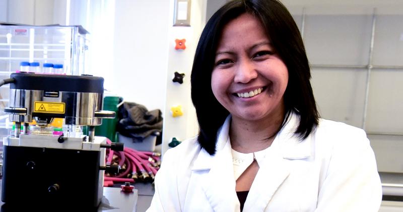 Ruby Sullan smiles while standing in a lab with taps and tubes on the walls.