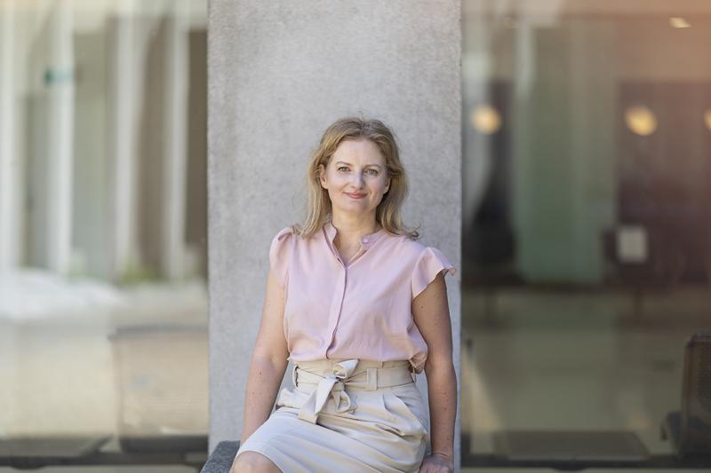 Jennifer Gommerman smiles, sitting in front of a concrete pillar outdoors.