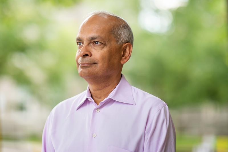 Vivek Goel smiles and looks thoughtful, standing in a park outdoors.