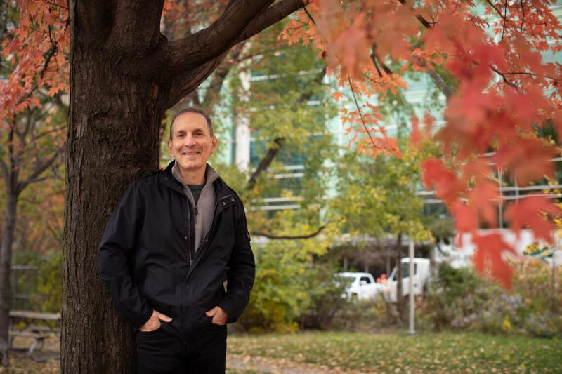 Daniel Drucker smiles as he leans on a tree in full fall colour.
