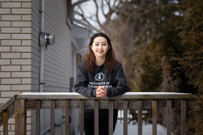 Melody Bagaa smiles as she leans on a snow-covered railing. She wears a University of Toronto sweatshirt.