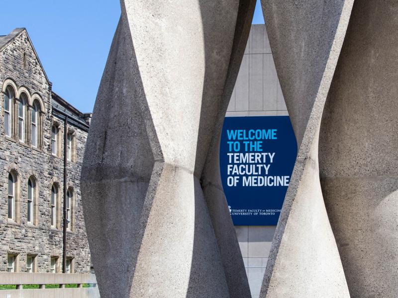 On a sunny day, a sign reading Temerty Faculty of Medicine is framed by an abstract stone sculpture.