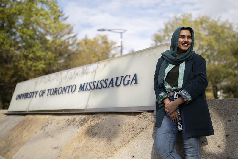 Amna Adnan laughs as she stands next to a large sign that says University of Toronto Mississauga.