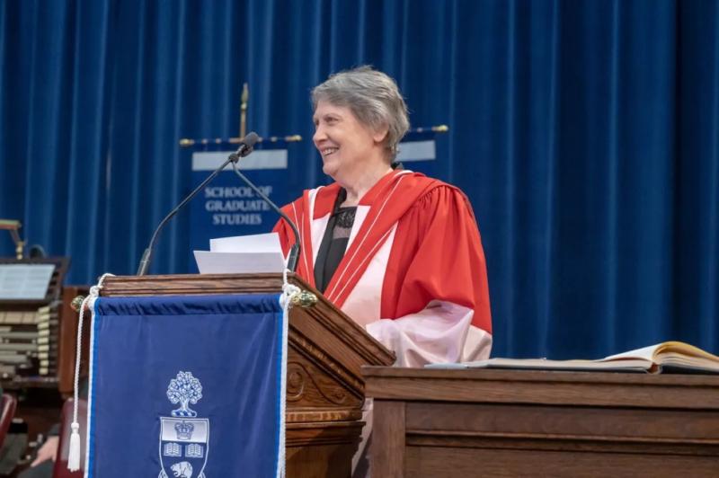 Helen Clark stands at a podium in a gown giving a speech at convocation.