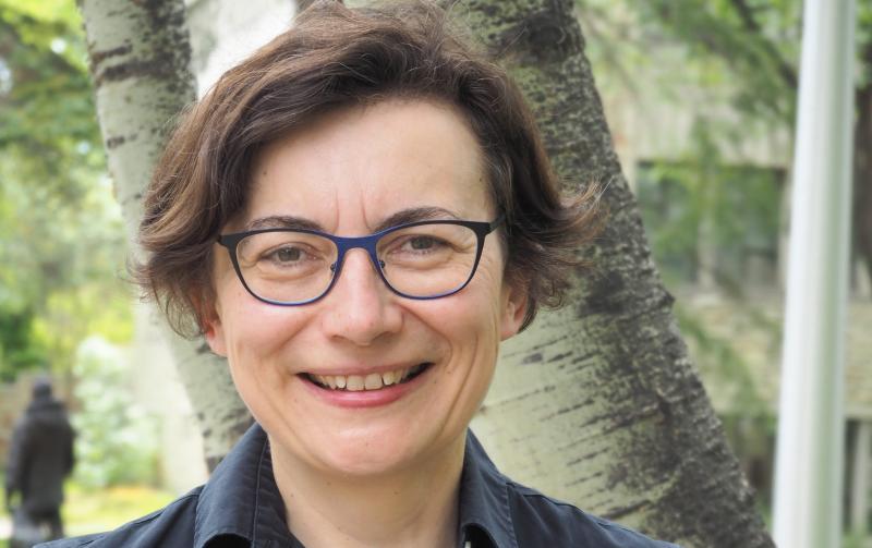 Valerie Korinek smiles while standing in front of a birch tree outdoors.