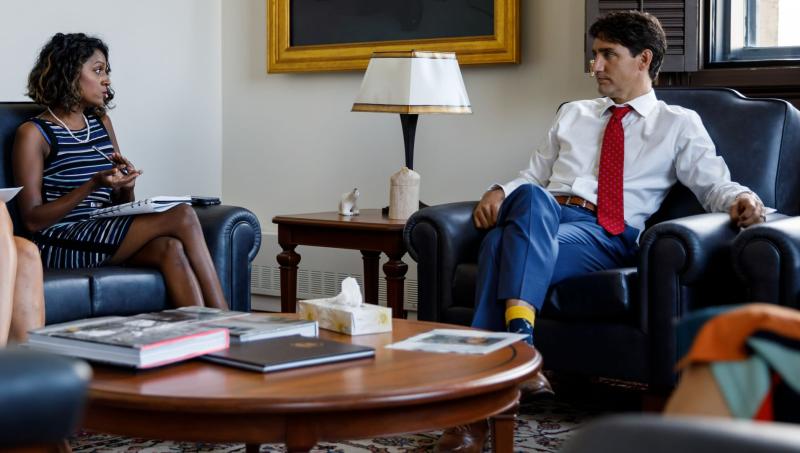 Vandana Fatima Kattar and Justin Trudeau sit in armchairs in an office, next to a table of books and documents.