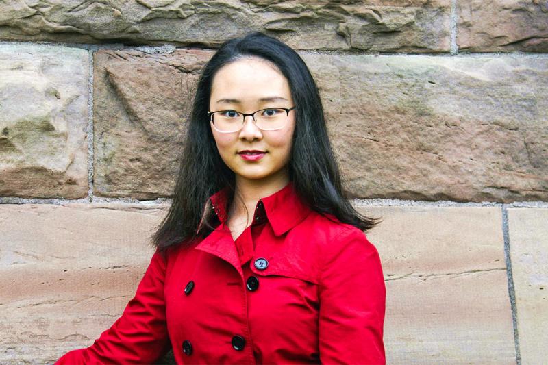 Zihan Gao smiles, standing in front of a stone wall outdoors.