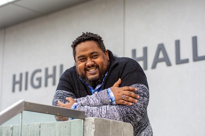 Keon Priestley smiles and laughs as he leans on the railing outside U of T Scarborough's Highland Hall.