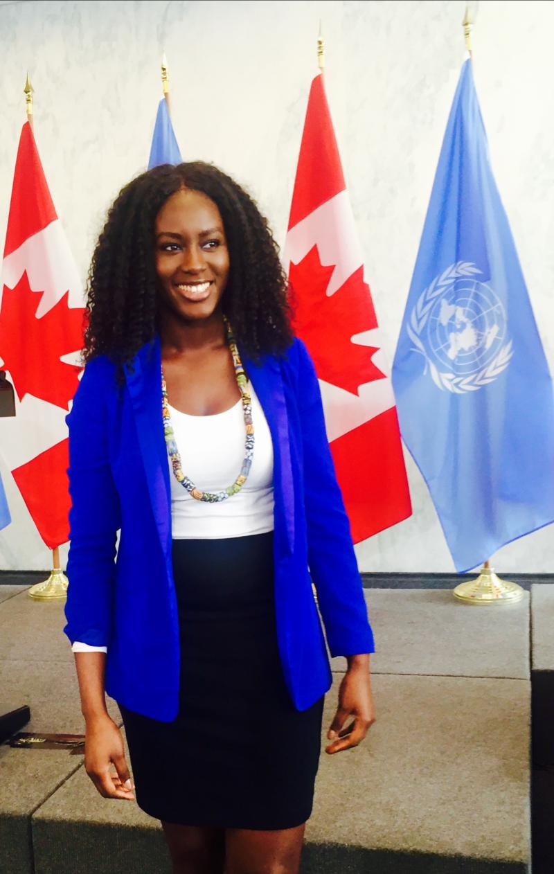 Binta Bajaha standing in front of two Canadian flags and two UN flags