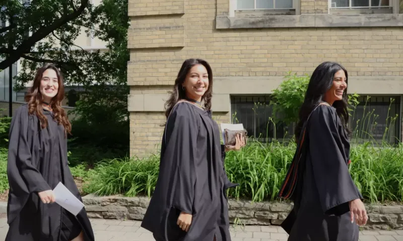 Three graduates wearing gowns and walking
