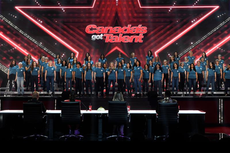 More than 50 women in identical t-shirts stand on a stage under a sign that reads, Canada's Got Talent.