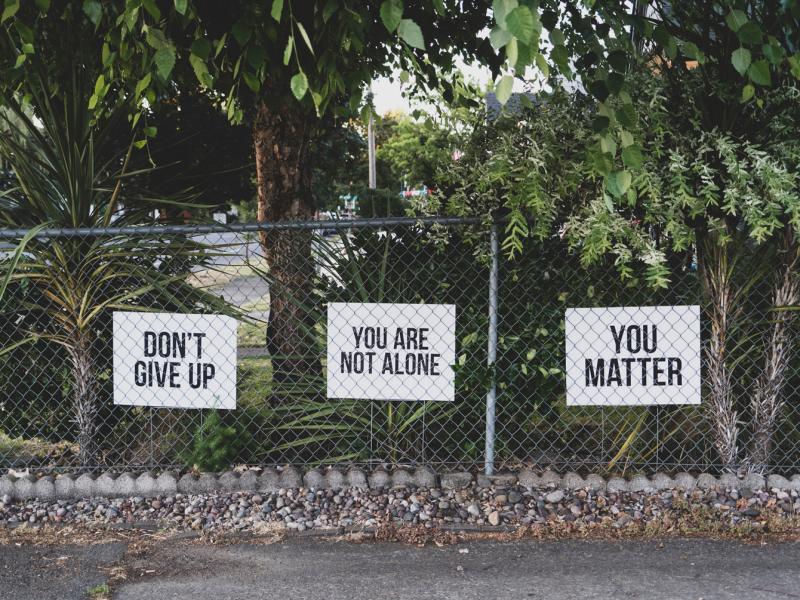 Three signs on a fence read: Don't give up, You are not alone, You matter.