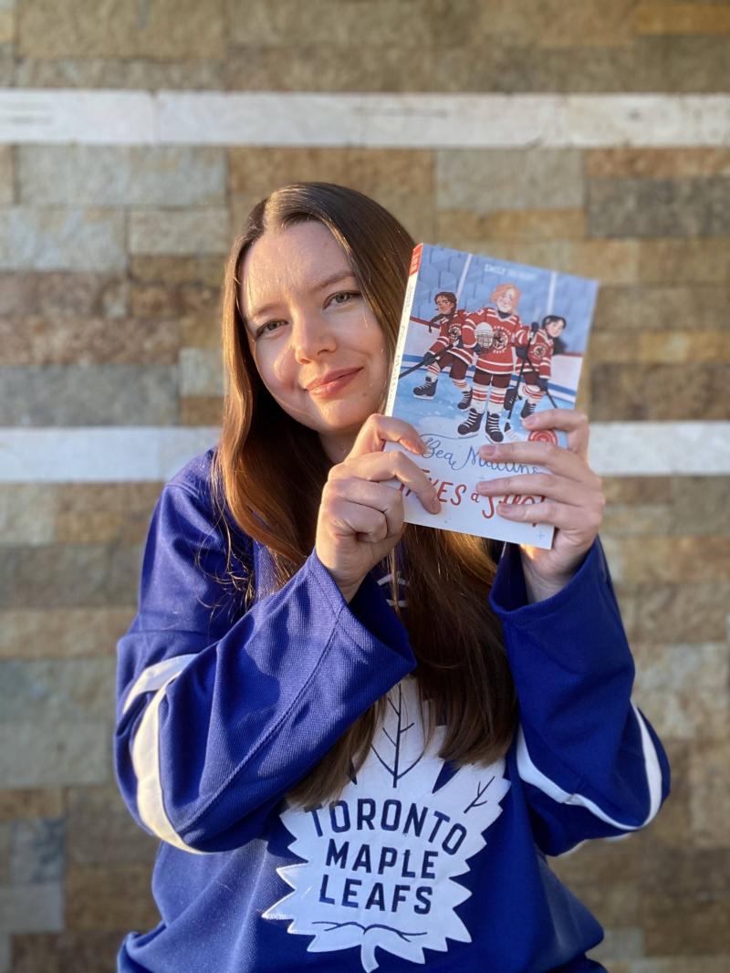 Emily wearing a Toronto Maple Leafs jersey and holding her book