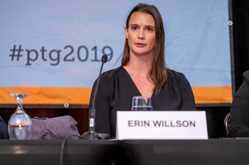 Erin Willson speaks as she sits at a conference table. On the screen behind is the hashtag #ptg2019. 