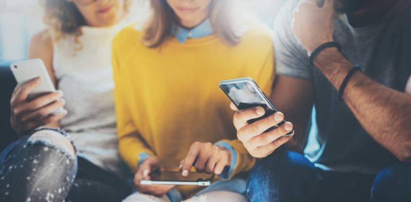 photo by Shutterstock of three students on their phone.