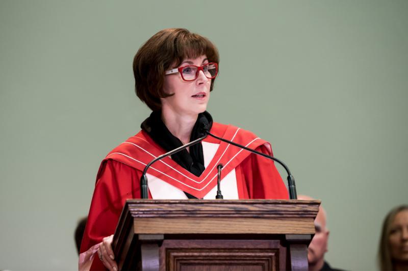 Katie Taylor, wearing academic robes, speaks at a lectern.